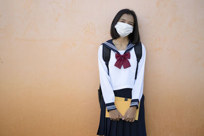 Portrait of girl wearing mask standing against wall