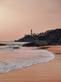 Lighthouse on beach by sea against sky during sunset