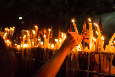 Cropped image of women lighting candles on railing at night