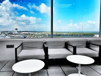 Empty chairs and table at airport against blue sky