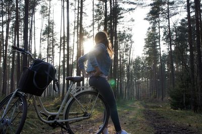 Woman sitting on bicycle against trees at forest
