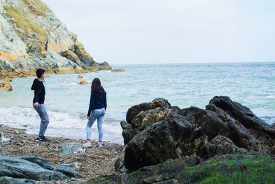 Rear view of people on rock by sea against sky