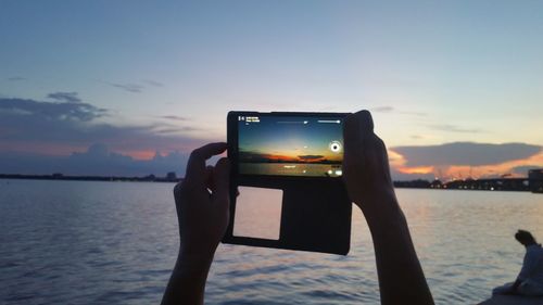Man photographing on mobile phone against sky during sunset