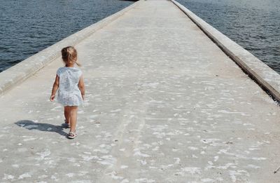 Rear view of girl walking on pier during sunny day