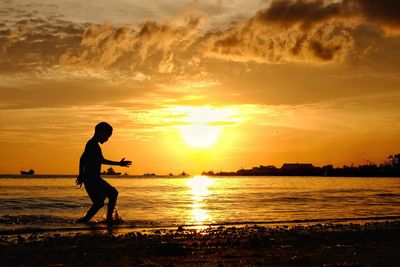 Silhouette man standing on beach against sky during sunset