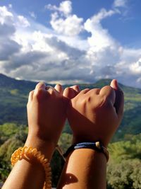 Close-up of hand holding hands against sky