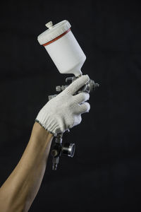 Cropped hand of person holding airbrush against black background