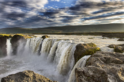 Scenic view of waterfall against clouds