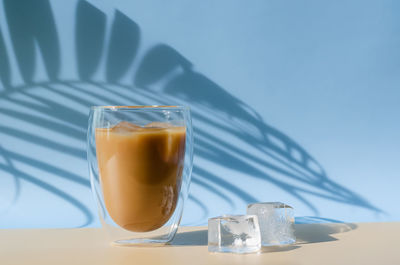 Iced latte coffee with iced cube on the floor and shadow from coconut leaf. summer drink concept.