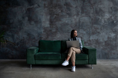 Young female designer sitting on green sofa in loft living room and drawing on tablet computer