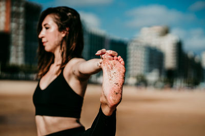 Side view of flexible female standing on sandy shore of river in extended hand to big toe pose and practicing yoga while balancing on leg with eyes closed