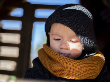 Close-up of cute girl wearing sweater and knit hat sitting at home