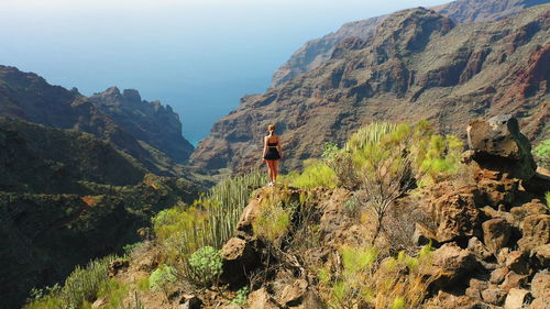 Bold girl on edge of mountain looking on gorge and ocean from above. hiking trail on tenerife.