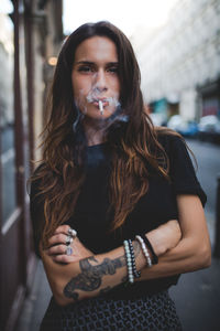 Portrait of young woman smoking while standing on footpath