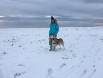 Full length of woman with dog standing on snow covered land against sky