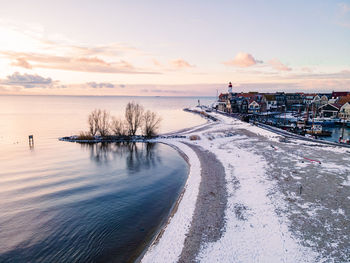 Snow covered city by sea against sky during sunset