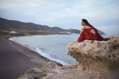 Woman on rock at beach against sky