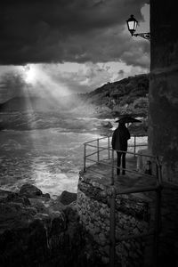 Rear view of man with umbrella looking at sea against sky