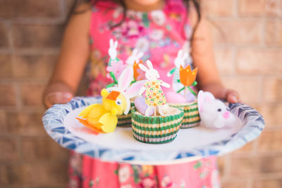 Midsection of girl holding plate with multi colored easter bunnies