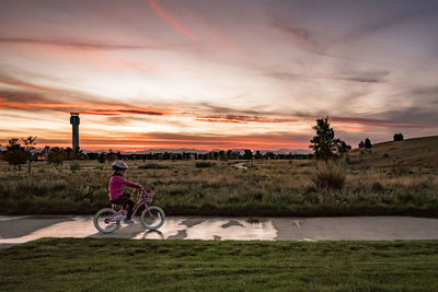 Young girl rides a bike along the sidewalk in a park at sunset