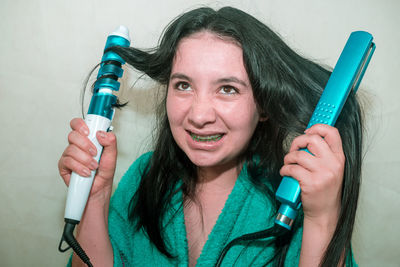 Close-up of young woman holding curling tongs and hair straightener