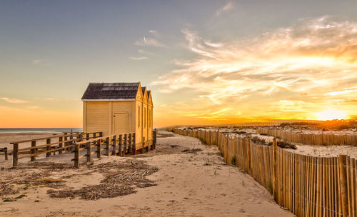 Wooden posts on beach against sky during sunset