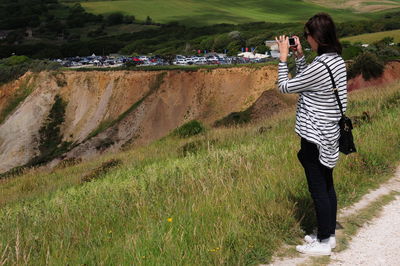 Full length side view of woman photographing while standing on cliff