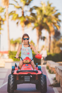 Portrait of girl riding toy car on footpath