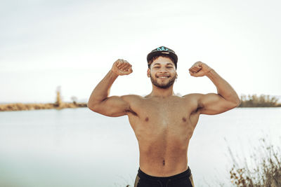 Smiling man flexing muscles while standing against clear sky