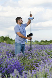 Surveyor using equipment on lavender field against cloudy sky