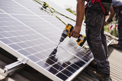 Electrician using power tool for installing solar panel on rooftop