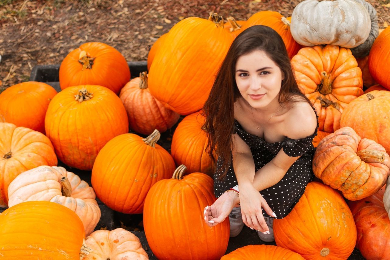 PORTRAIT OF A SMILING YOUNG WOMAN WITH ORANGE PUMPKINS