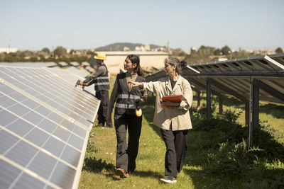 Female entrepreneur examining solar panels while walking with engineer at power station