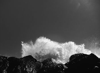 Low angle view of waves splashing on rocks against sky