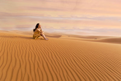 Woman in yellow dress playing with the wind in the desert ii