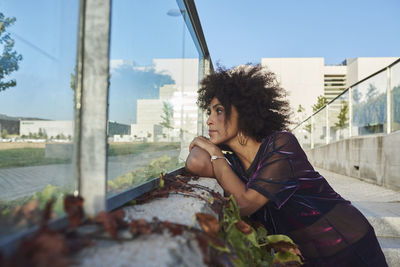 Portrait of beautiful young woman sitting in city against sky