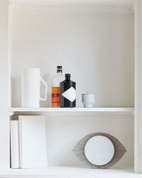 Still of bottles, books in bright, white, clean modern kitchen shelf