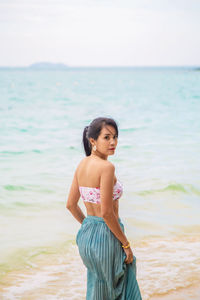  asian woman in bikini with dress standing in front of the sea and looking at a camera 
