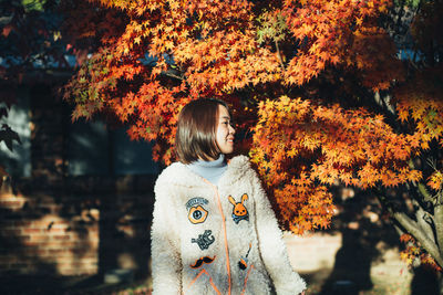 Portrait of young woman standing by tree during autumn