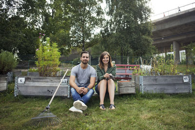 Full length of happy friends sitting on grass against trees