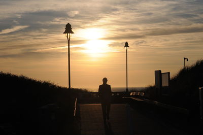 Rear view of silhouette man standing on street against sky during sunset