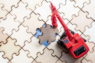 High angle view of red toy crane picking jigsaw piece