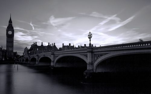 Arch bridge over river against cloudy sky