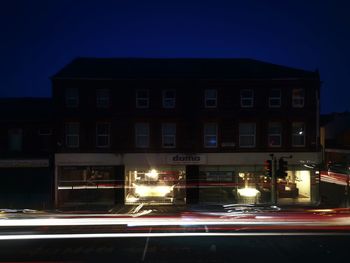 Light trails on road by building against sky at night