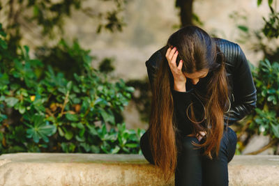 Woman wearing jacket with head in hand sitting outdoors