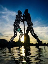 Silhouette men standing by water against sky during sunset