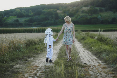 Mother holding hand of son wearing space suit while walking at field