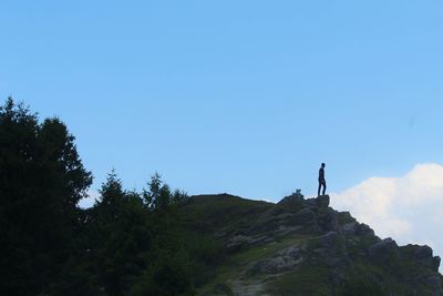 Low angle view of silhouette young man standing on mountain against blue sky