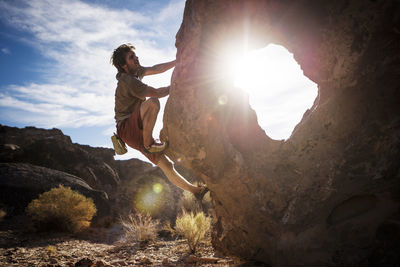 Man climbing rock against sky on sunny day