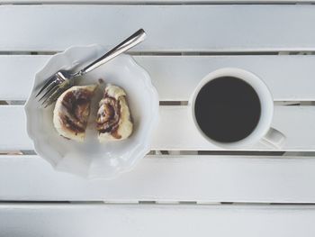 Directly above shot of cinnamon roll in bowl with black coffee on wooden table